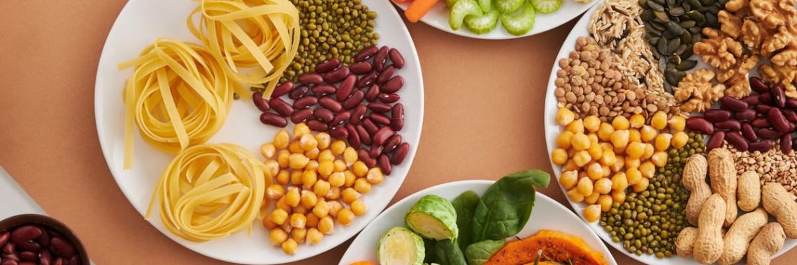 A vibrant mix of legumes, vegetables, nuts, and pasta arranged on white plates showcasing a balanced, healthy diet.
